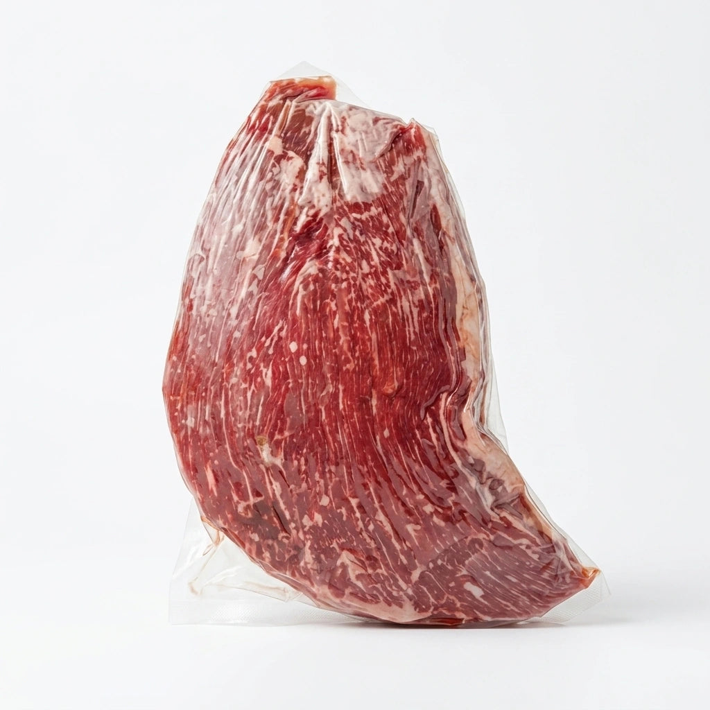 A vacuum-sealed flank steak with visible marbling, photographed against a clean white studio background.
