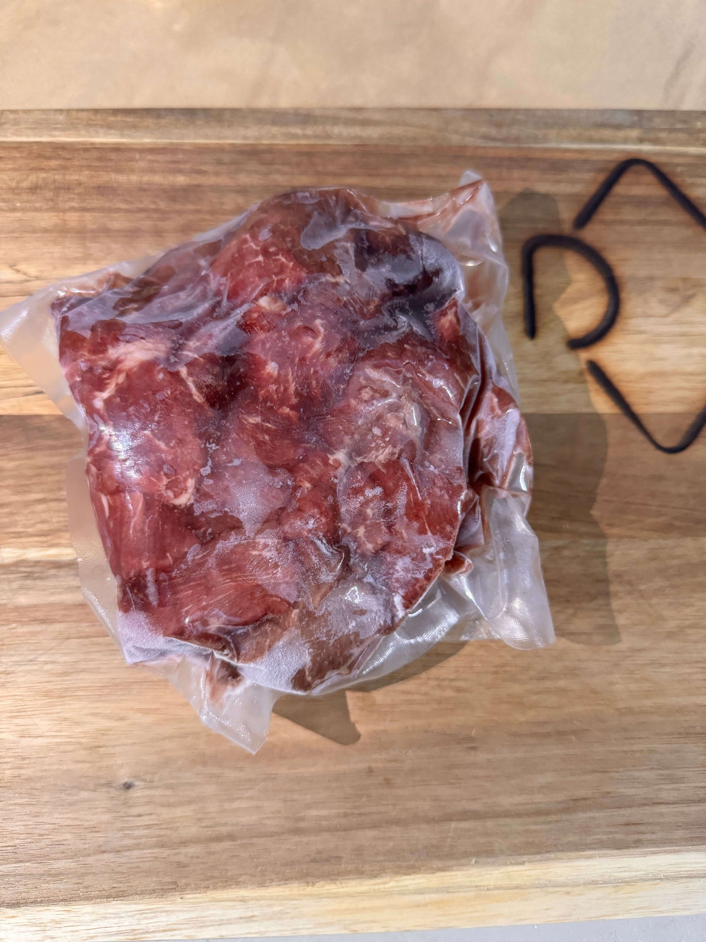 Vacuum-sealed piece of raw stew meat on a wooden board. The clear plastic packaging tightly wraps the meat, highlighting its fresh texture.