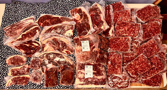 1/8 vacuum-sealed packs of grass-fed beef cuts and ground beef from Diamond D Ranch displayed on a patterned surface.