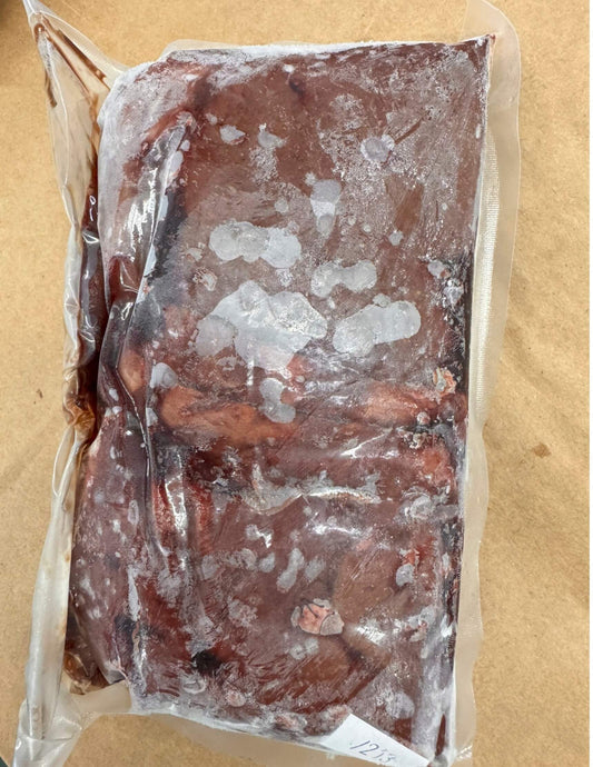 A vacuum-sealed package of frozen beef liver with noticeable frost, lying on a brown paper surface. The texture suggests ice crystals and a cold environment.