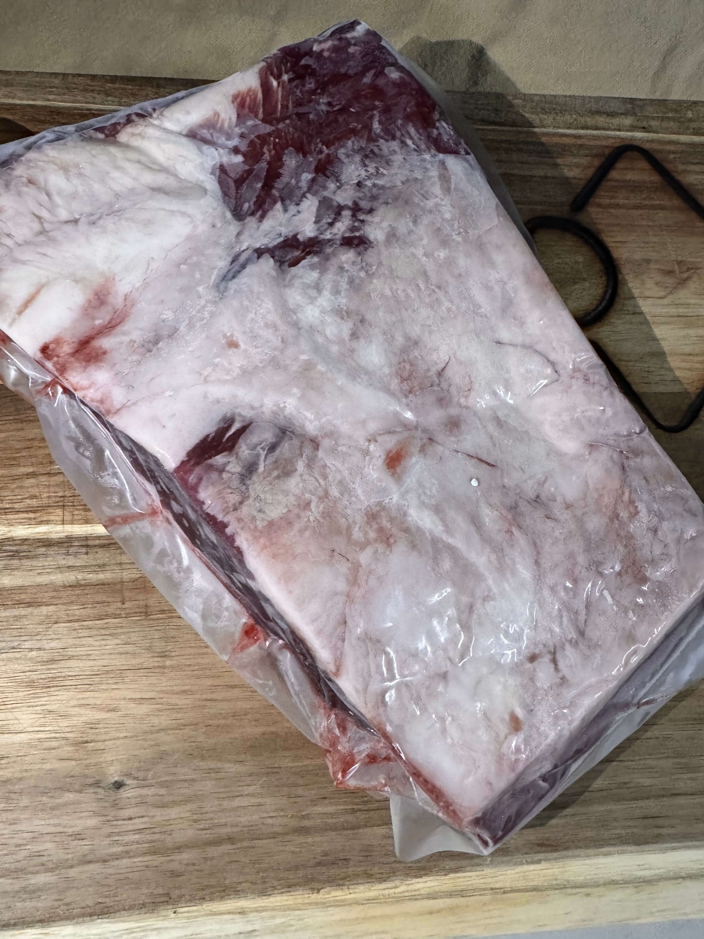 Raw beef brisket in vacuum-sealed packaging on a wooden cutting board. The meat has a thick fat layer, showcasing marbling; the scene conveys freshness.