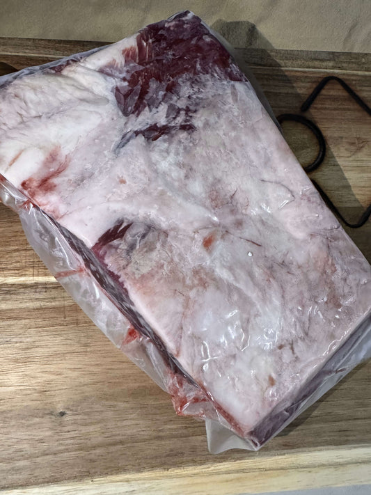 Raw beef brisket in vacuum-sealed packaging on a wooden cutting board. The meat has a thick fat layer, showcasing marbling; the scene conveys freshness.