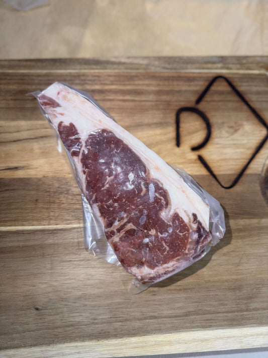 A vacuum-sealed ribeye steak on a wooden cutting board. The marbled meat is well-defined against the light wood, creating a fresh and appetizing appearance.