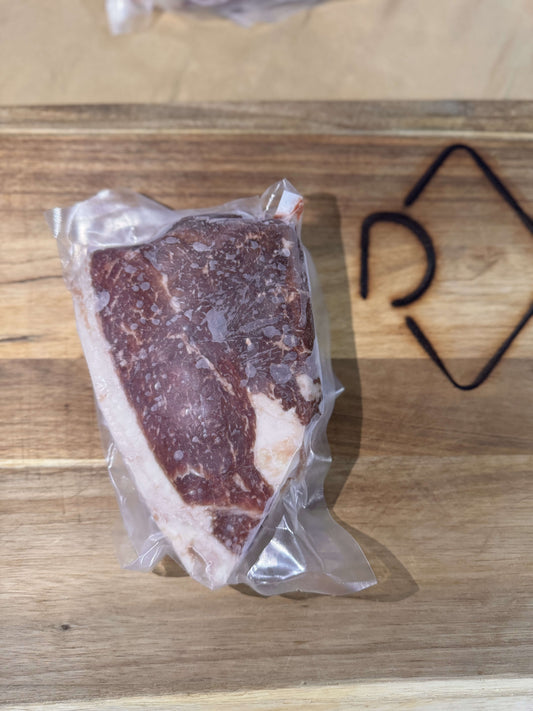 A vacuum-sealed piece of marbled sirloin steak rests on a wooden cutting board. The background features a geometric design. The scene feels fresh and rustic.