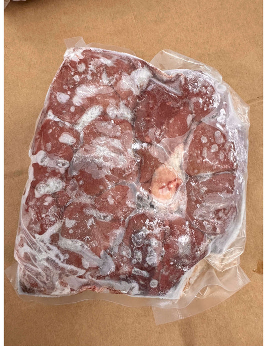 Frozen chunks of beef kidney sealed in a clear plastic bag, with frost covering the surface. The bag rests on brown paper, conveying a raw and cold appearance.
