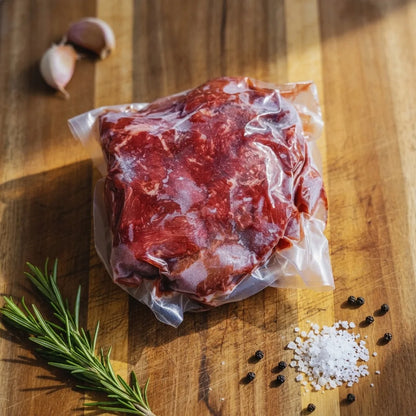 Grass-fed beef stew meat in vacuum packaging with rosemary, garlic and sea salt on wood