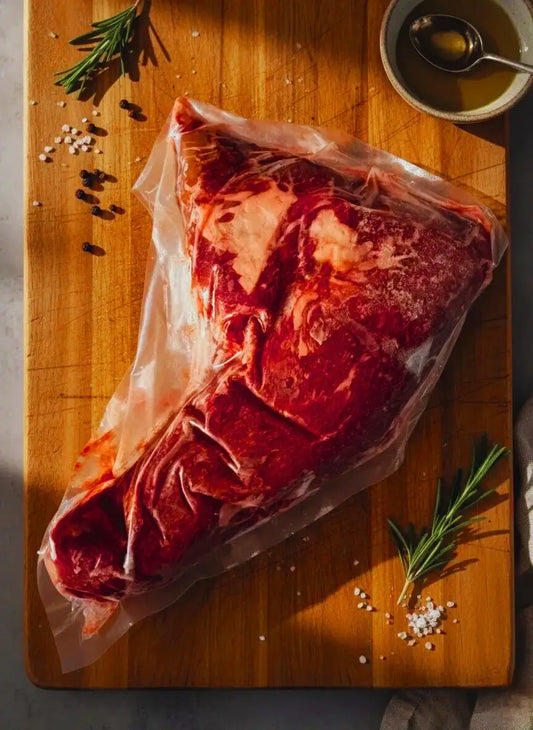 Diamond D Ranch vacuum-sealed raw tri tip roast on a wooden board with rosemary, salt, pepper.