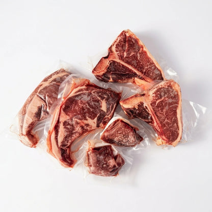 Several raw beef or lamb chops with visible fat marbling, individually sealed in clear plastic vacuum packaging, arranged on a plain white background.