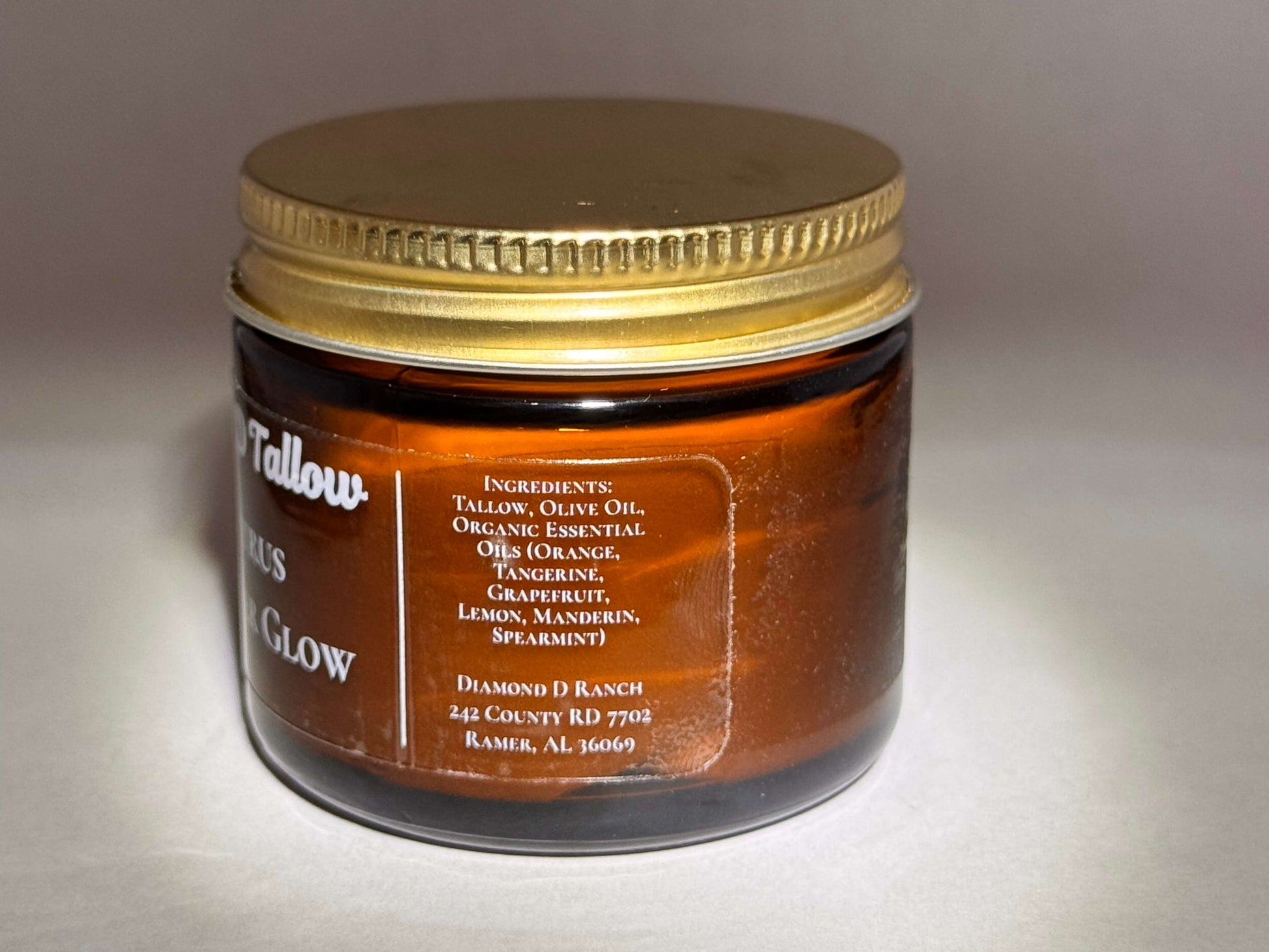 A brown glass jar with a gold lid labeled "Tallow Citrus Glow." Ingredients like tallow, olive oil, and essential oils are listed. Simple, earthy tone.