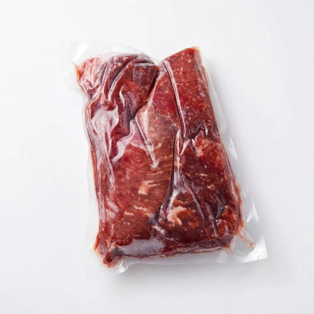 Vacuum-sealed pack of cubed steak pieces on a white background, overhead view