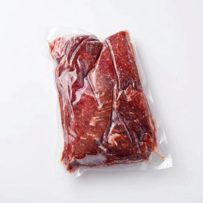 Vacuum-sealed pack of cubed steak pieces on a white background, overhead view
