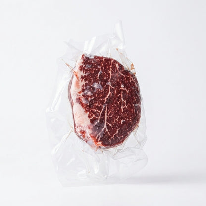 A raw filet mignon vacuum-sealed in clear plastic packaging, centered on a clean white background.