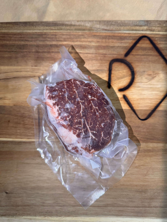 Vacuum-sealed marbled filet mignon steak on a wooden cutting board; the sun creates a geometric shadow. The raw meat is rich in color, conveying freshness.