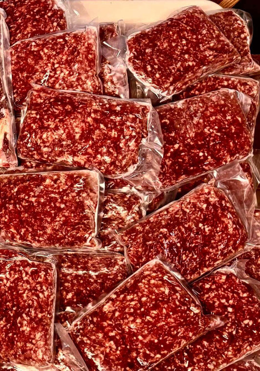 Plastic-wrapped packs of ground meat are stacked, displaying a marbled texture. The image conveys a sense of abundance and freshness in Diamond D Ranch.