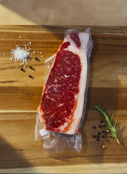 Diamond D Ranch vacuum-sealed raw New York Strip Steak cut on a wooden board, showcasing marbling and fresh quality.