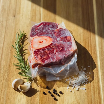 Vacuum-sealed osso buco on a sunlit wooden board with rosemary, garlic, and sea salt