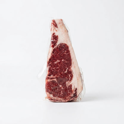 Raw ribeye steak with heavy marbling, vacuum sealed upright on a white background