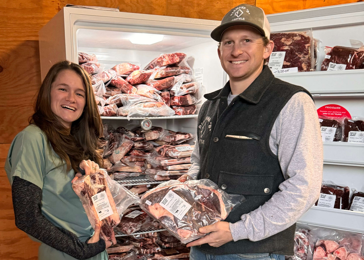 A smiling Sydney and Dalton holding packaged cuts of meat quality beef from Diamond D Ranch in front of the freezer filled with more quality meat packages.