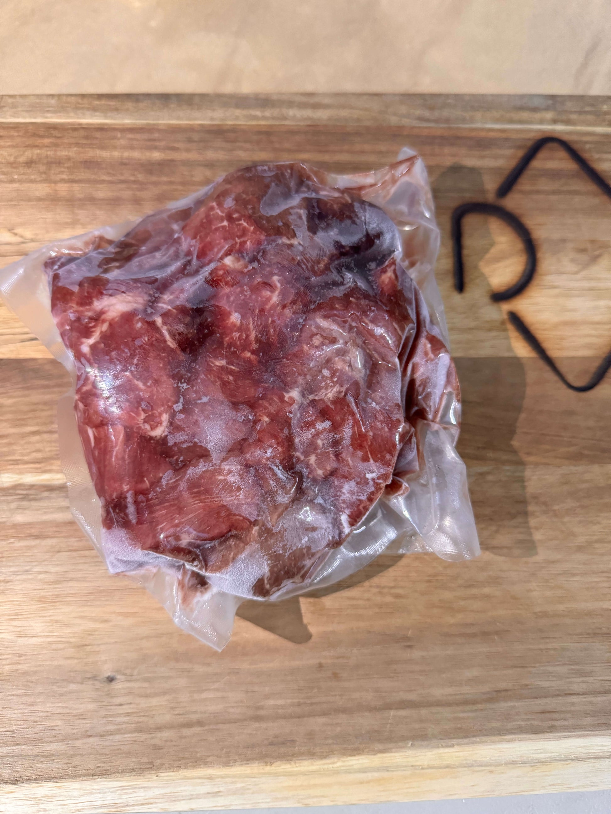 Vacuum-sealed piece of raw stew meat on a wooden board. The clear plastic packaging tightly wraps the meat, highlighting its fresh texture.