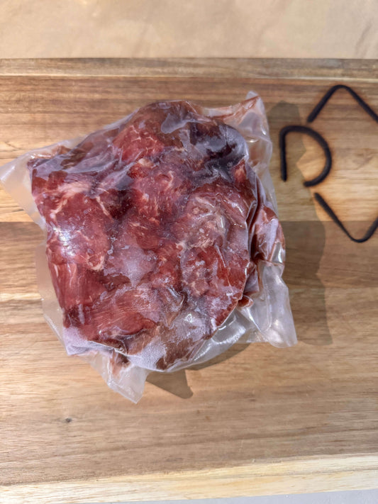 Vacuum-sealed piece of raw stew meat on a wooden board. The clear plastic packaging tightly wraps the meat, highlighting its fresh texture.