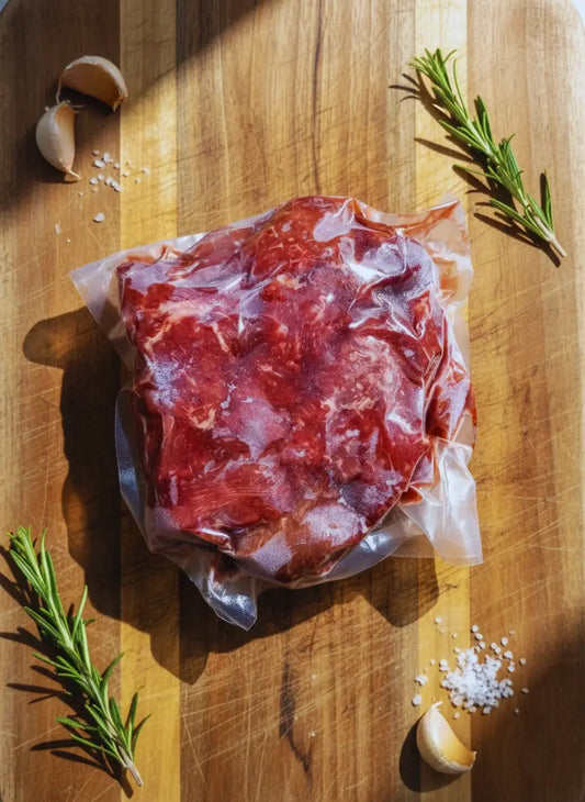 Diamond D Ranch vacuum-sealed raw beef stew & tips on a wooden board, clear wrap showing fresh texture and quality.