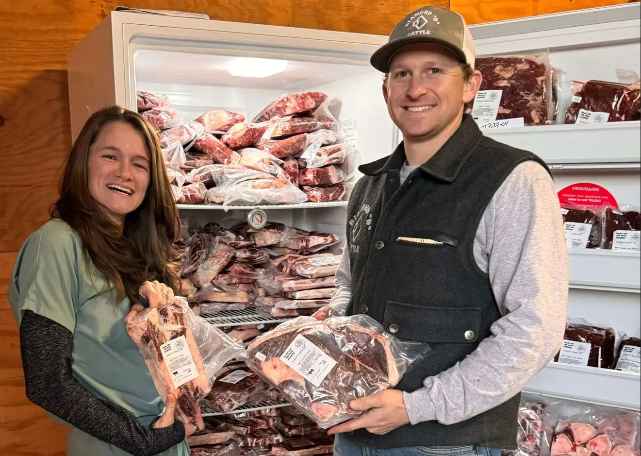 Sydney and Dalton are holding packages of Diamond D Ranch beef in front of a refrigerator filled with more meat.