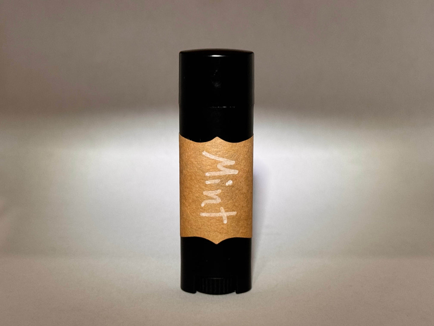 A black tube with a brown paper label reading "Mint" in white handwriting stands vertically on a neutral background, creating a simple and natural look.