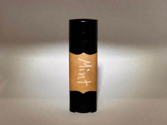 A black tube with a brown paper label reading "Mint" in white handwriting stands vertically on a neutral background, creating a simple and natural look.
