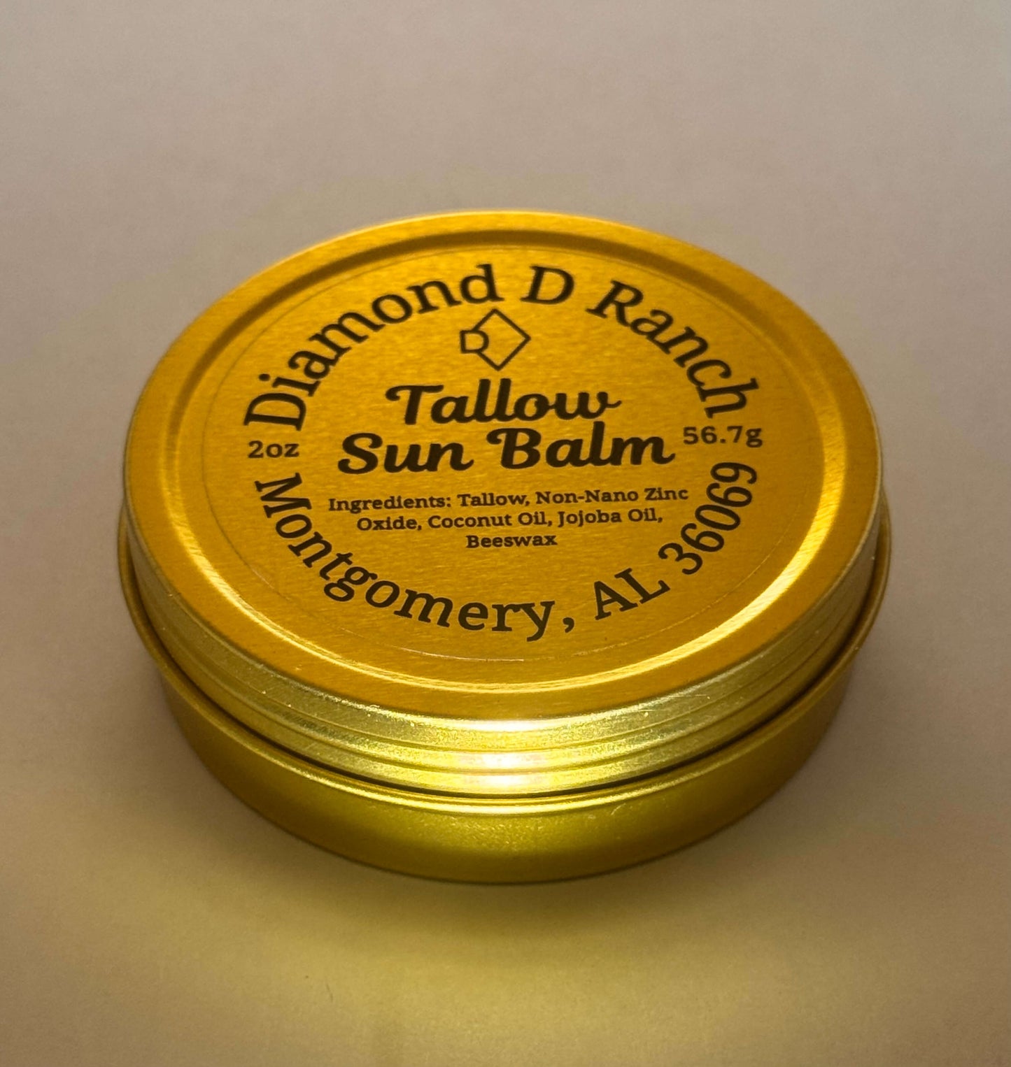 A gold tin labeled "Diamond D Ranch Tallow Sun Balm" with ingredients like tallow, zinc oxide, coconut and jojoba oils, beeswax; 56.7g; Montgomery, AL.