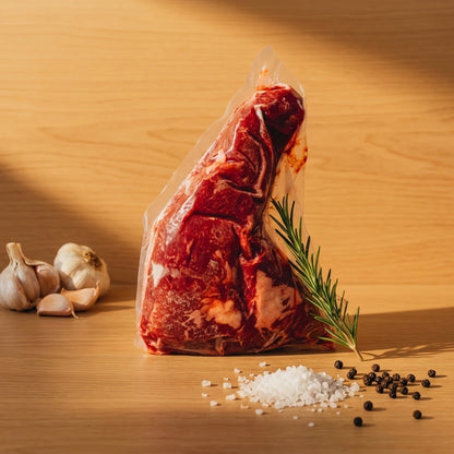 Grass-fed tri tip roast in vacuum packaging with garlic bulbs, rosemary and sea salt