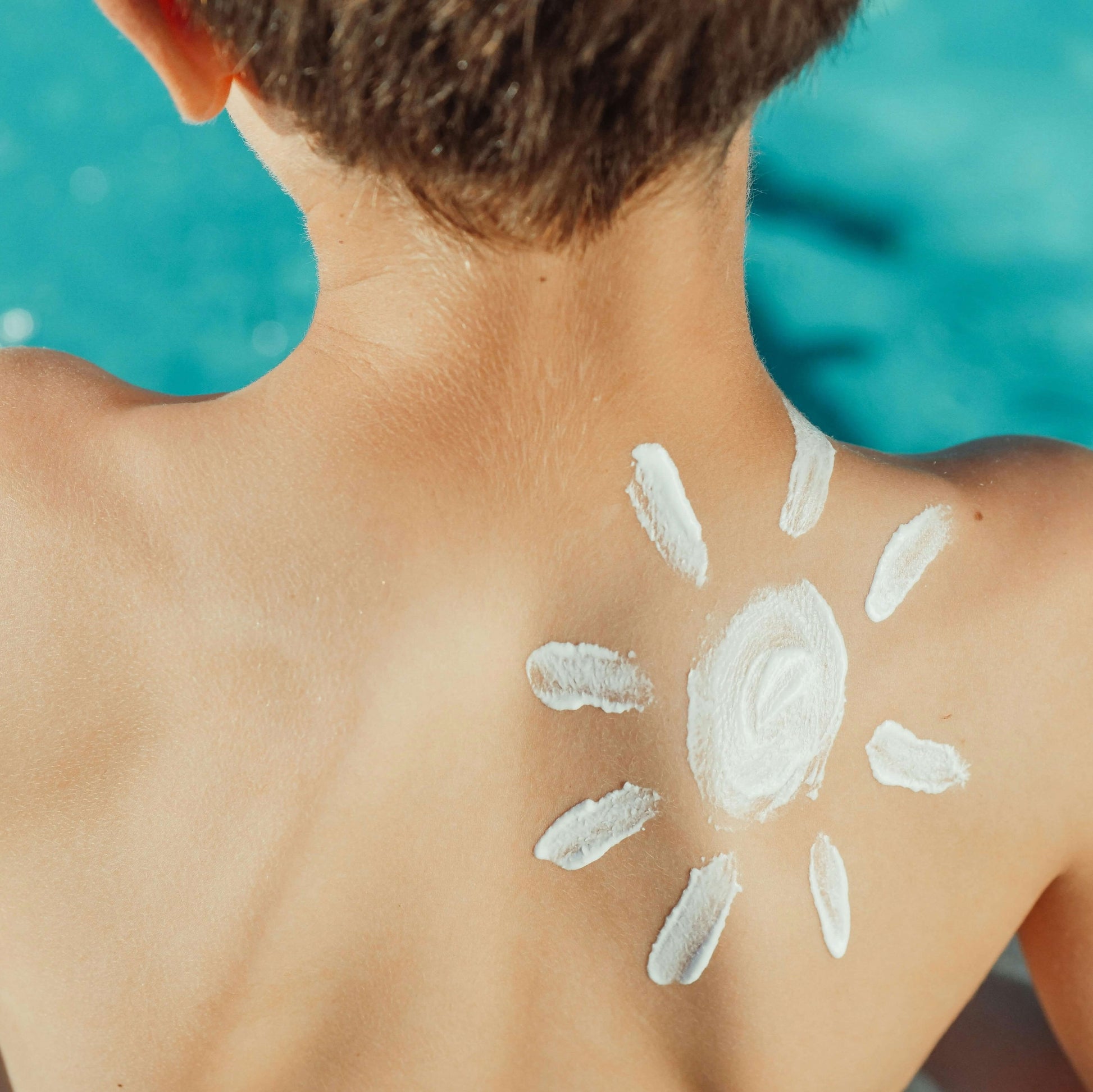 Child facing a blue pool with whipped tallow in a sun shape on their back. The scene conveys a feeling of summer fun and skin protection.